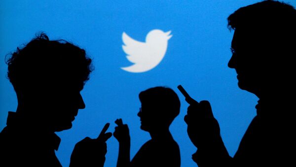 People holding mobile phones are silhouetted against a backdrop projected with the Twitter logo in this illustration picture taken September 27, 2013 - Sputnik International