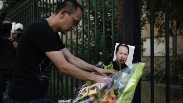 A member of the Chinese commmunity arranges a display of flowers besides a photograph of slain Chinese tailor Zhang Chaolin during a candlelight vigil in Aubervilliers on August 7, 2017, on the first anniversary of the fatal mugging of the Chinese tailor. Chinese tailor Zhang Chaolin, aged 49, was assaulted by three men in the streets in Aubervilliers on August 7, 2016 and died 5 days later from a coma. - Sputnik International