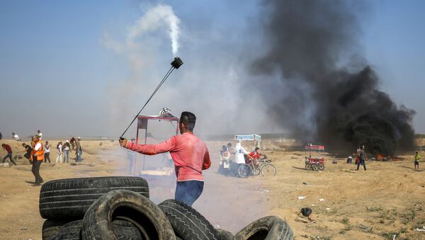A Palestinian protester uses a slingshot to throw back a tear gas canister towards Israeli forces during clashes following a demonstration along the border east of Gaza City on July 6, 2018 - Sputnik International