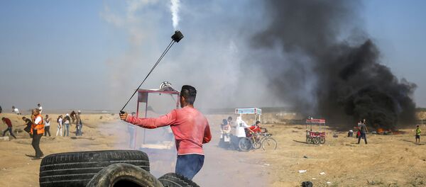 A Palestinian protester uses a slingshot to throw back a tear gas canister towards Israeli forces during clashes following a demonstration along the border east of Gaza City on July 6, 2018 - Sputnik International
