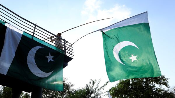 A boy uses a bamboo stick to adjust national flags at an overhead bridge ahead of Pakistan's Independence Day, in Islamabad, Pakistan August 10, 2018 - Sputnik International