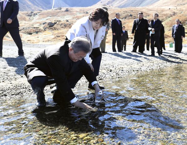 South Korean President Moon Jae-in puts water from the crater lake into a bottle as his wife Kim Jung-sook watches on Mount Paektu - Sputnik International