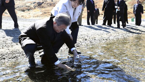 South Korean President Moon Jae-in puts water from the crater lake into a bottle as his wife Kim Jung-sook watches on Mount Paektu - Sputnik International