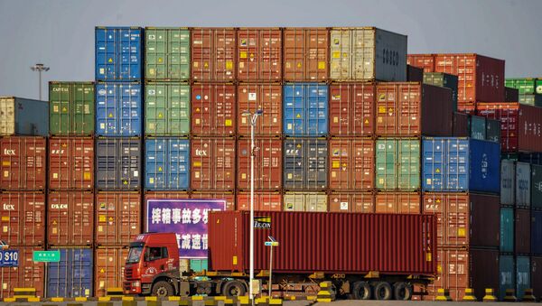 A truck transports a container next to stacked containers at a port in Qingdao in China's eastern Shandong province on October 12, 2018 - Sputnik International