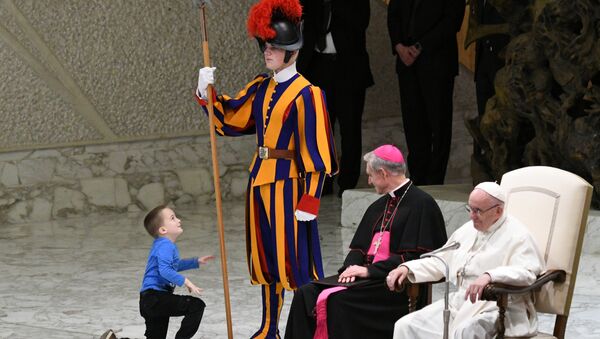 Prefect of the Papal Household, Georg Ganswein (C) watches a boy who came from the audience onto the stage, play with a Swiss Guard's spear as Pope Francis (R) looks on during the weekly general audience on November 28, 2018 in Paul VI hall at the Vatican. - Sputnik International