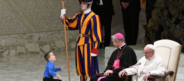 Prefect of the Papal Household, Georg Ganswein (C) watches a boy who came from the audience onto the stage, play with a Swiss Guard's spear as Pope Francis (R) looks on during the weekly general audience on November 28, 2018 in Paul VI hall at the Vatican. Prefect of the Papal Household, Georg Ganswein (C) watches a boy who came from the audience onto the stage, play with a Swiss Guard's spear as Pope Francis (R) looks on during the weekly general audience on November 28, 2018 in Paul VI hall at the Vatican. - Sputnik International