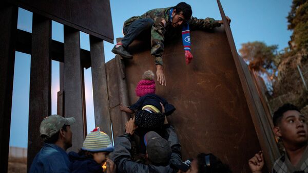 Migrants from Honduras, part of a caravan of thousands from Central America trying to reach the United States, try to jump a border fence to cross illegally from Mexico to the U.S, in Tijuana, Mexico, December 2, 2018 - Sputnik International