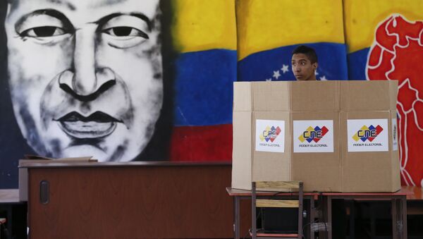 A voter chooses his candidate next to a mural of late Venezuelan President Hugo Chavez during presidential elections in Caracas, Venezuela - Sputnik International