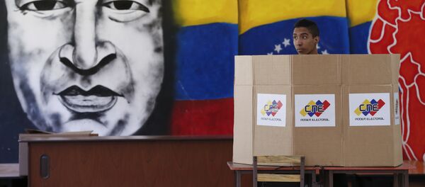 A voter chooses his candidate next to a mural of late Venezuelan President Hugo Chavez during presidential elections in Caracas, Venezuela - Sputnik International