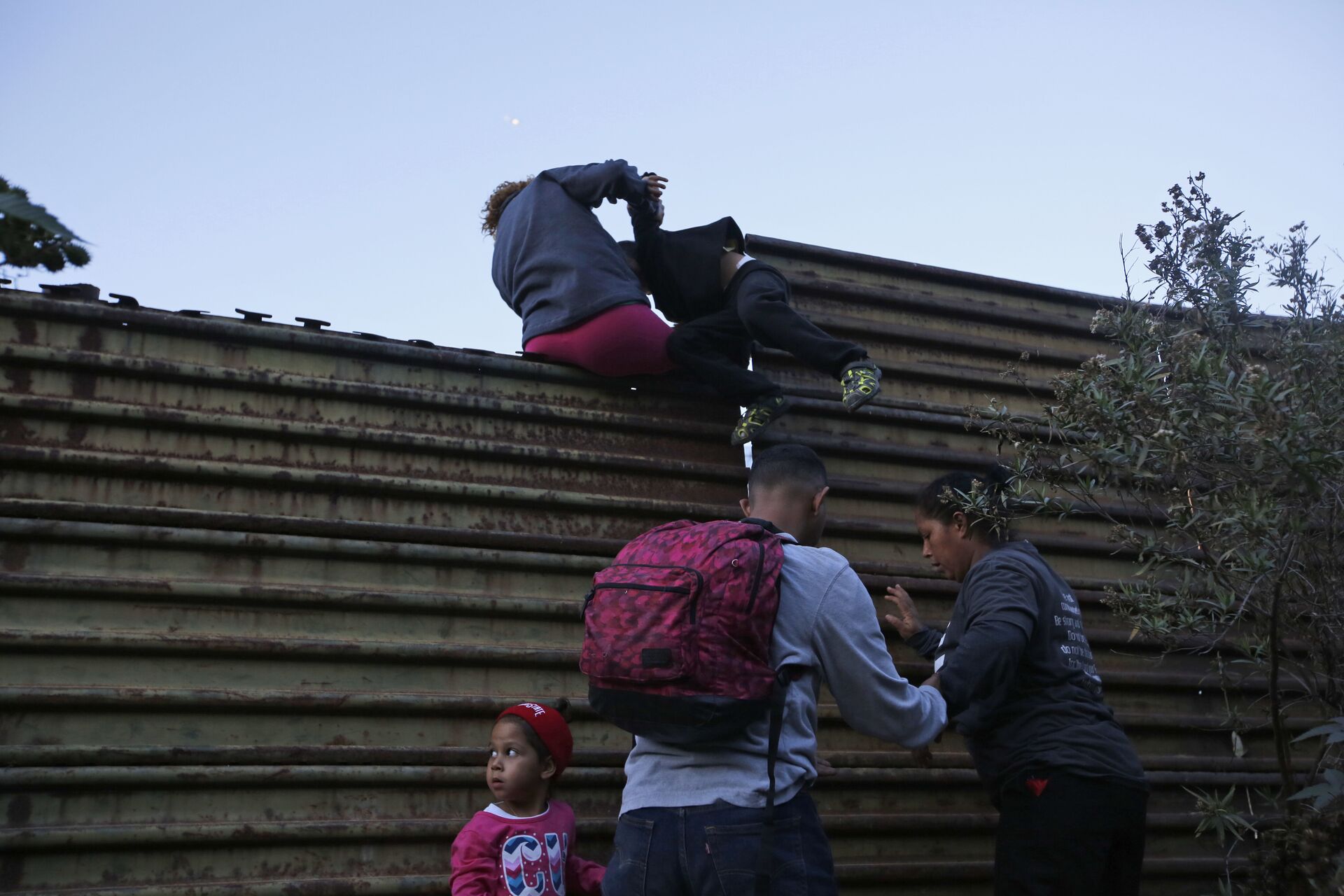Honduran migrants help each other to cross over the U.S. border wall to San Diego, California, from Tijuana, Mexico, Saturday, Dec. 15, 2018 - Sputnik International, 1920, 26.09.2022