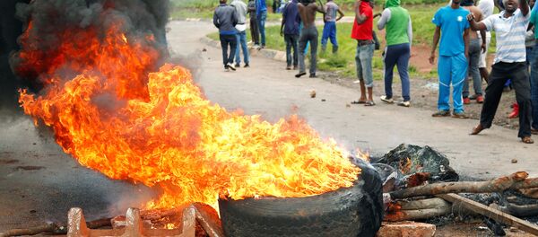 Protesters stand behind a burning barricade during protests on a road leading to Harare, Zimbabwe, January 15, 2019 Protesters stand behind a burning barricade during protests on a road leading to Harare, Zimbabwe, January 15, 2019 - Sputnik International