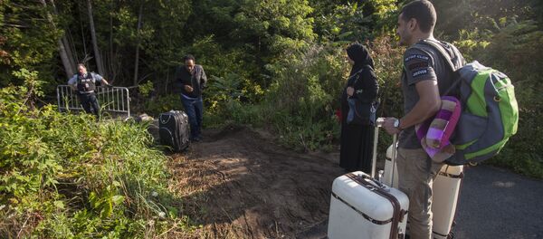 RCMP officers speaks with migrants as they prepare to cross the US/Canada border illegally near Hemmingford, Quebec, August 20, 2017 - Sputnik International