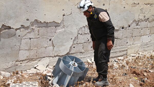 A member of the Syrian civil defence volunteers, also known as the White Helmets, stands next to the tail fin of a bomb as local bomb-disposal experts search for unexploded ordnance in a rebel-held area of Daraa on July 20, 2017 - Sputnik International