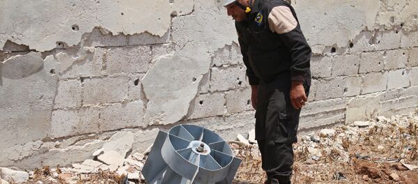 A member of the Syrian civil defence volunteers, also known as the White Helmets, stands next to the tail fin of a bomb as local bomb-disposal experts search for unexploded ordnance in a rebel-held area of Daraa on July 20, 2017 - Sputnik International