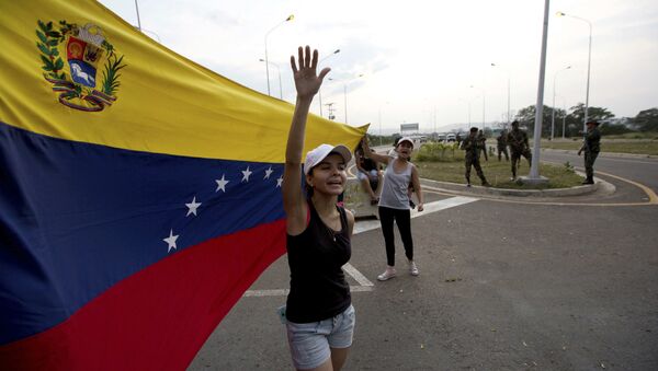 Woman shouts Welcome humanitarian aid as he waives Venezuelan flag in front aof a group of Venezuelan Army soldiers and National Guard officers blocking the main access to the Tienditas International Bridge that links Colombia and Venezuela, near Urena, Venezuela, Thursday, Feb. 7, 2019 - Sputnik International