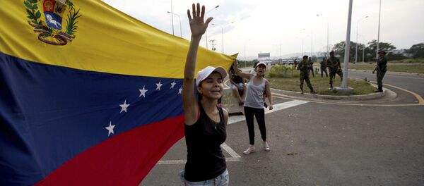 Woman shouts Welcome humanitarian aid as he waives Venezuelan flag in front aof a group of Venezuelan Army soldiers and National Guard officers blocking the main access to the Tienditas International Bridge that links Colombia and Venezuela, near Urena, Venezuela, Thursday, Feb. 7, 2019 Woman shouts Welcome humanitarian aid as he waives Venezuelan flag in front aof a group of Venezuelan Army soldiers and National Guard officers blocking the main access to the Tienditas International Bridge that links Colombia and Venezuela, near Urena, Venezuela, Thursday, Feb. 7, 2019 - Sputnik International