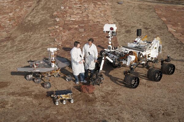 Two spacecraft engineers stand with three generations of Mars rovers developed at NASA JPL, Pasadena, Ca. Front and center is a flight spare of Sojourner, left is a working sibling to Spirit and Opportunity, right is test rover Curiosity. - Sputnik International