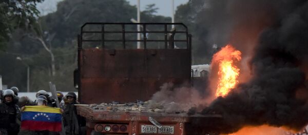 Venezuelan security forces display a national flag next to a truck which was burnt during the weekend when trying to enter the country with humanitarian aid, during clashes with supporters of Venezuelan opposition leader Juan Guaido on the Venezuelan side of the Francisco de Paula Santander International Bridge, as seen from Cucuta, Colombia, on February 25, 2019. - Sputnik International