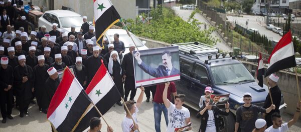 Druze men carry Syrian flags and pictures of Syrian President Bashar Assad during a rally marking Syria's Independence Day, in the Druze village of Ein Qiniyye, Israeli-controlled Golan Heights, Tuesday, April 17, 2018. - Sputnik International