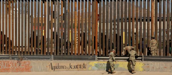 U.S. soldiers walk next to the border fence between Mexico and the United States, as migrants are seen walking behind the fence, after crossing illegally into the U.S. to turn themselves in, in El Paso, Texas, U.S., in this picture taken from Ciudad Juarez, Mexico, April 3, 2019 - Sputnik International