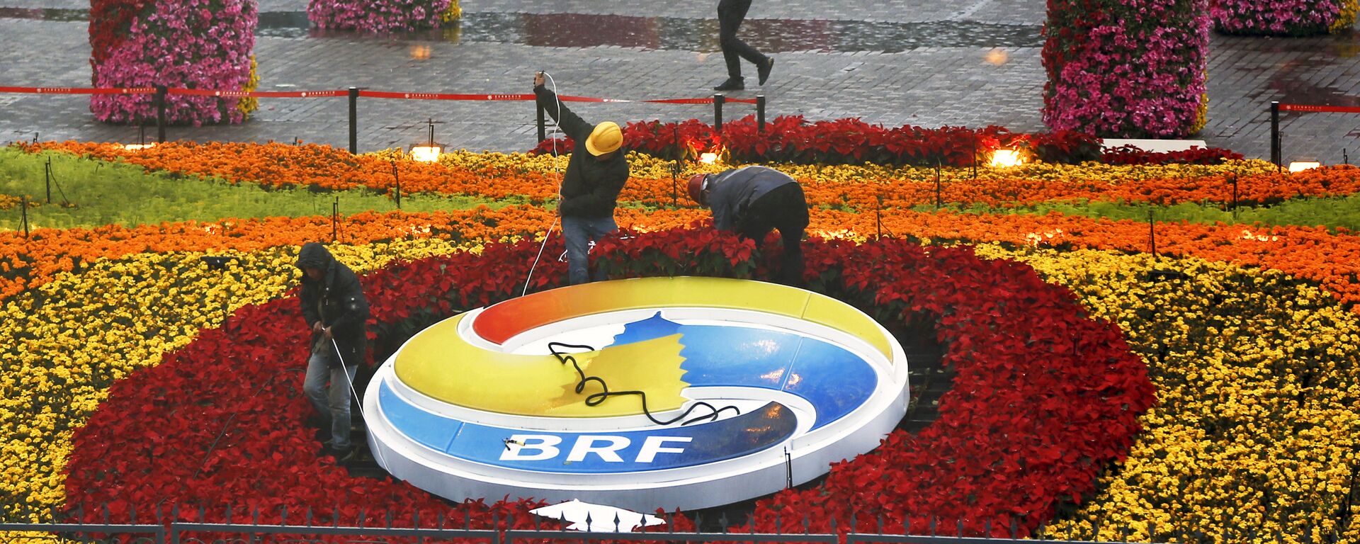 A man carrying an umbrella to shield from the rain as workers dismantle the Belt and Road Forum logo outside the media center as leaders are attending the round table summit of the Belt and Road Forum chaired by Chinese President Xi Jinping in Beijing, Saturday, April 27, 2019 - Sputnik International, 1920, 05.07.2019