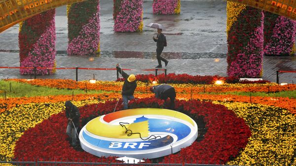 A man carrying an umbrella to shield from the rain as workers dismantle the Belt and Road Forum logo outside the media center as leaders are attending the round table summit of the Belt and Road Forum chaired by Chinese President Xi Jinping in Beijing, Saturday, April 27, 2019 - Sputnik International