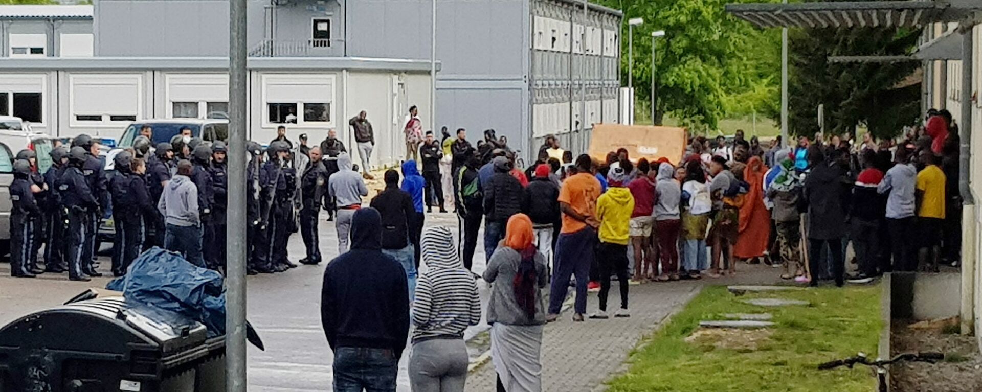 German police officers and migrants stand in front of an asylum center after a woman was found dead in the center in Regensburg, Germany, Saturday, May 11, 2019 - Sputnik International, 1920, 26.11.2021