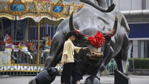 A woman pulls a 2 wheel trolley loaded with goods touches a bull statue on display outside a retail and wholesale clothing mall in Beijing, Monday, July 9, 2018 - Sputnik International