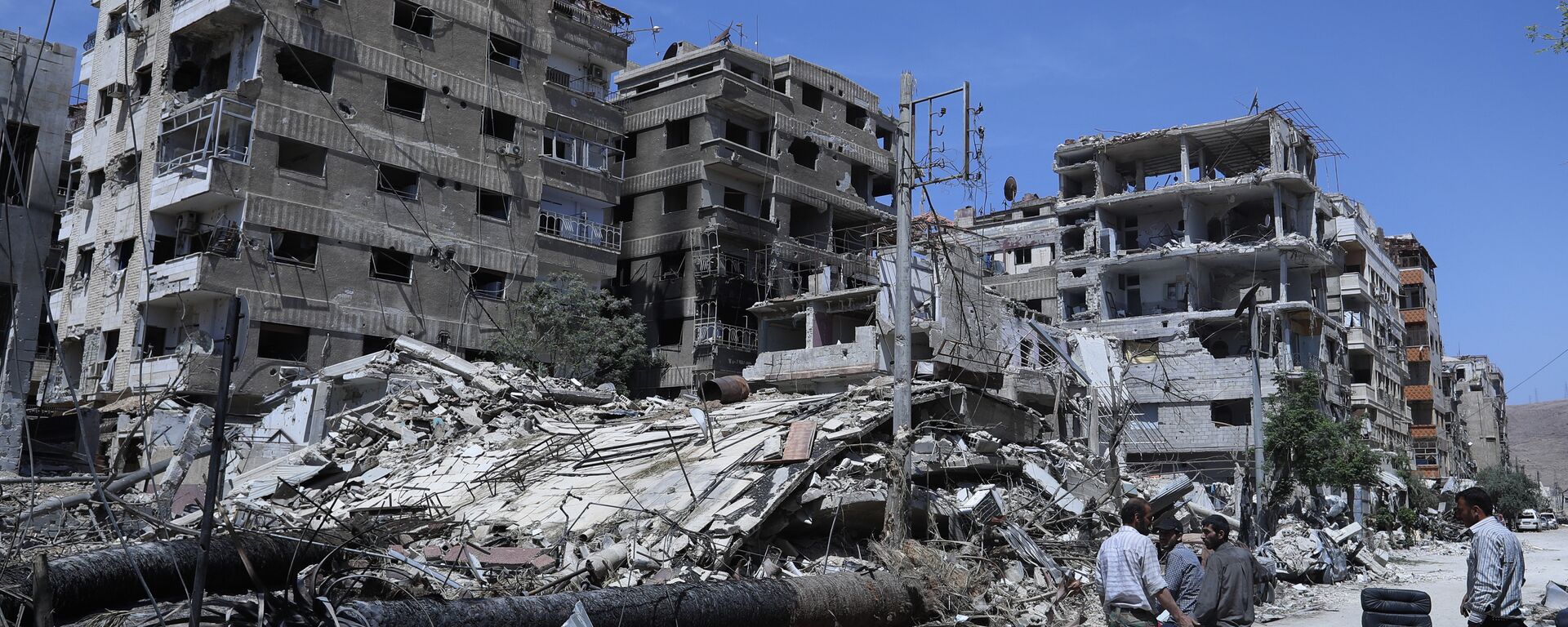 Syrians stand in front of damaged buildings in the Damascus suburb of Douma, the site of an alleged chemical weapons attack, 16 April 2018 - Sputnik International, 1920, 21.01.2020