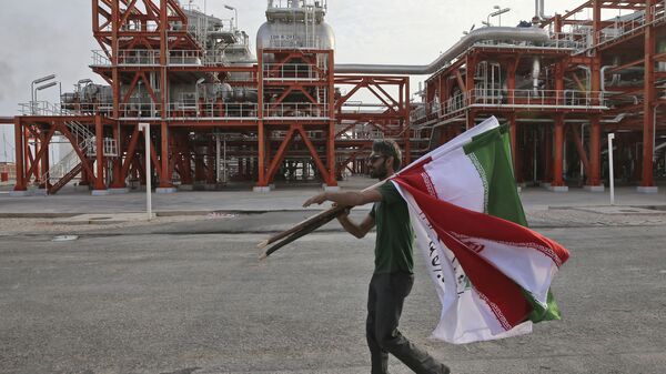 An Iranian worker carries Iranian flags prior to an inauguration ceremony of a natural gas refinery at the South Pars gas field on the northern coast of the Persian Gulf, in Asaluyeh, Iran - Sputnik International