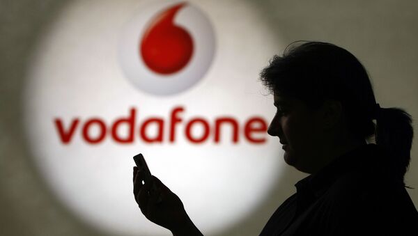 A woman looks at a mobile phone on 19 July ]2007, in Duesseldorf before a logo of the mobile operator Vodafone. - Sputnik International