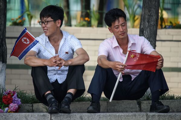 Two Men Sit Holding North Korean and Chinese Flags Near Kim Il Sung Square in Pyongyang - Sputnik International