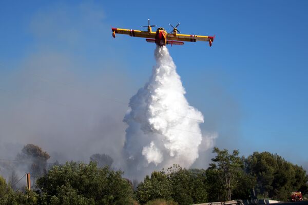 A Canadair firefighting plane drops water over a fire which broke out in the industrial zone of Vitrolles, southeastern France, on July 10, 2019.  - Sputnik International