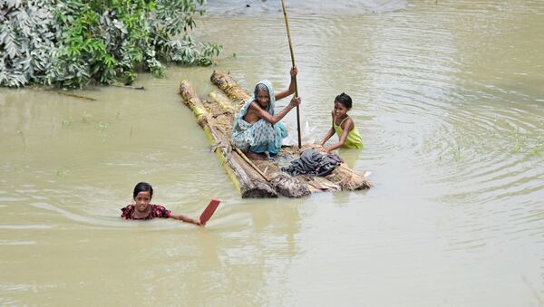 A woman rows a makeshift raft as girls wade through flood waters at the Laharighat village in Morigaon district, in the northeastern state of Assam, India, July 21, 2019 - Sputnik International