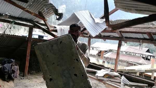 A resident shows a riddled metal suitcase as he stands under a damaged roof of a house in Salkhala village, in Neelum Valley - Sputnik International