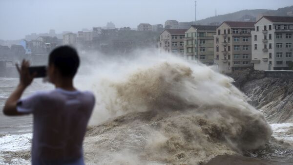 In this Aug. 9, 2019, photo released by Xinhua News Agency, a man uses his mobile phone to record waves crashing on the shore as typhoon Lekima approaches the Shitang Township of Wenling City in eastern China's Zhejiang Province. - Sputnik International