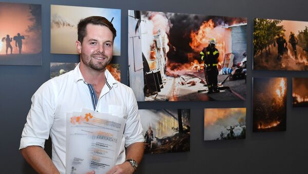 South Africa's Justin Sullivan poses for a photo with his work in the background after receiving 1st place in Top News, Single nomination and 2nd place in My Planet, Series nomination at the Andrey Stenin International Press Photo Contest Exhibition, in Moscow, Russia, November 8, 2018. The Andrei Stenin International Photo Contest is an annual contest for young photojournalists aged between 18 and 33 years old. - Sputnik International