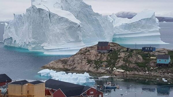 A picture taken on July 13, 2018 shows an iceberg behind houses and buildings after it grounded outside the village of Innarsuit, an island settlement in the Avannaata municipality in northwestern Greenland. - Sputnik International
