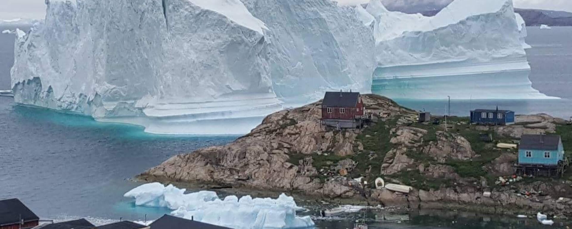 A picture taken on July 13, 2018 shows an iceberg behind houses and buildings after it grounded outside the village of Innarsuit, an island settlement in the Avannaata municipality in northwestern Greenland. - Sputnik International, 1920, 09.12.2020
