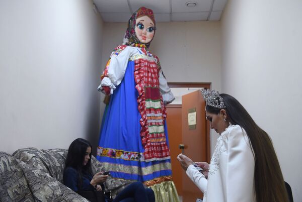 A participant in white is seen texting in a back room standing next to a human-sized doll dressed in traditional Russian attire. - Sputnik International