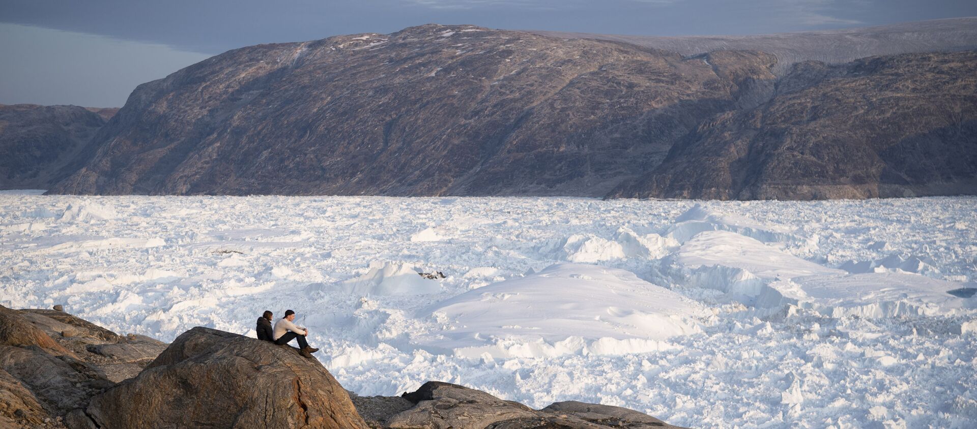 In this Aug. 16, 2019, photo, New York University student researchers sit on a rock overlooking the Helheim glacier in Greenland. - Sputnik International, 1920, 30.11.2019