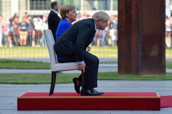 German Chancellor Angela Merkel and British Prime Minister Boris Johnson sit for the national anthems during a ceremony with military honours at the Chancellery on Johnson's first foreign visit since taking office on August 21, 2019 in Berlin - Sputnik International