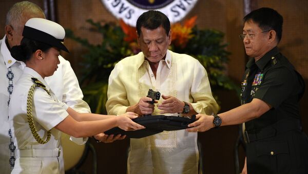 Philippine President Rodrigo Duterte (C) holds a .45 caliber handgun, one of 3,000 units handed over during a ceremonial turn-over to the military, at Malacanang Palace in Manila on July 18, 2017 - Sputnik International