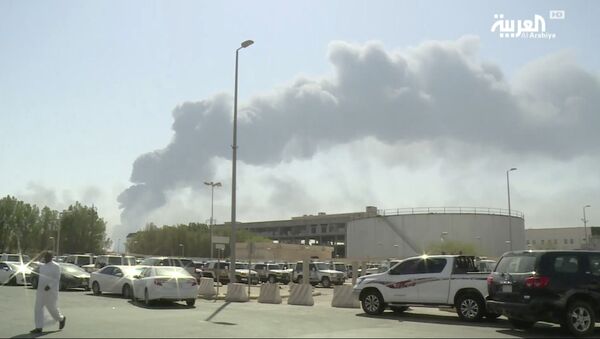 In this image, made from a video broadcast on the Saudi-owned Al-Arabiya satellite news channel on Saturday, 14 Sept. 2019, a man walks through a parking lot as the smoke from a fire at the Abqaiq oil processing facility can be seen behind him in Buqyaq, Saudi Arabia. Drones launched by Yemen's Houthi rebels struck the world's largest oil processing facility in Saudi Arabia and another major oil field Saturday, sparking huge fires at a vulnerable chokepoint for global energy supplies. - Sputnik International