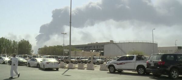 In this image made from a video broadcast on the Saudi-owned Al-Arabiya satellite news channel on Saturday, Sept. 14, 2019, a man walks through a parking lot as the smoke from a fire at the Abqaiq oil processing facility can be seen behind him in Buqyaq, Saudi Arabia. Drones launched by Yemen's Houthi rebels attacked the world's largest oil processing facility in Saudi Arabia and another major oilfield Saturday, sparking huge fires at a vulnerable chokepoint for global energy supplies - Sputnik International