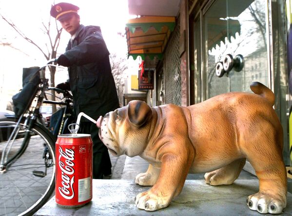 A Chinese postal worker leaves with his bike after delivering mail to a fashion salon decorated with a porcelain dog drinking a US soda out of a straw 16 February 2000 in Beijing. - Sputnik International