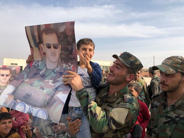 Syrian army soldiers hold placard depicting President of Syria Bashar al-Assad as Syrian government army troops rolled into Manbij, Syria, a flashpoint town west of the Euphrates River that Turkey had been aiming to capture and wrest from Kurdish control. Syrian forces moved into the area as part of a deal that has seen regime troops deploy in several Kurdish-controlled areas in Syria's north to protect the region from an assault by Turkish forces. - Sputnik International