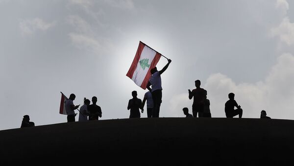 Anti-government protesters wave a Lebanese flag, as they stand on the Dome City Center known as The Egg, an unfinished cinema leftover from the civil war, as they watch other protesters, in downtown Beirut, Lebanon, Sunday, Oct. 20, 2019. - Sputnik International