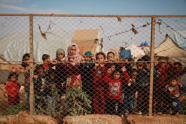 Displaced Syrian children stand behind a fence outside their tents in a camp set up near the village of Kafr Lusin, in Idlib's northern countryside near the Syria-Turkey border, on October 22, 2019. - Sputnik International