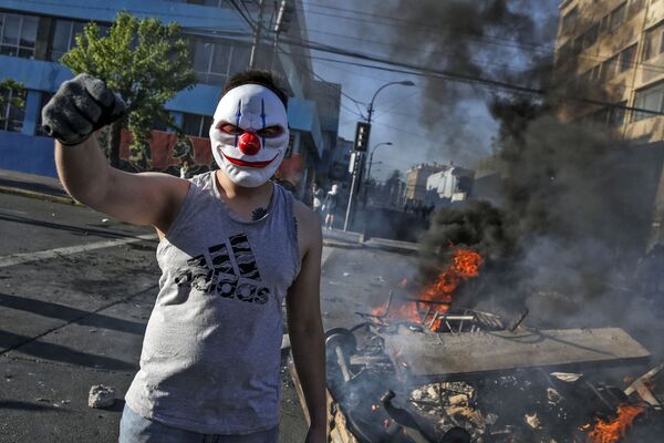 A masked demonstrator raises his clenched fist at a burning barricade during protests in Valparaiso, Chile, on October 20, 2019.  - Sputnik International